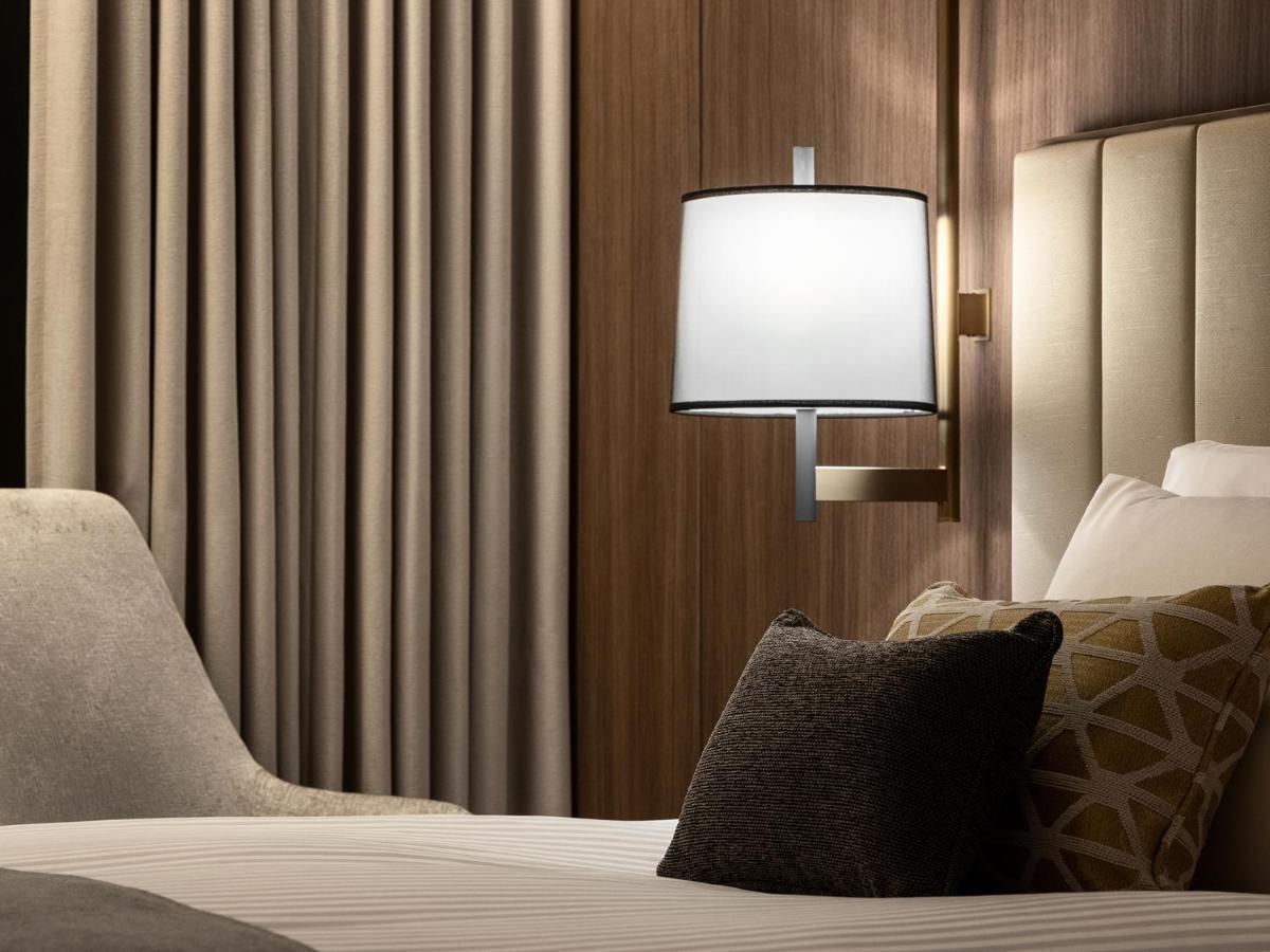 Mitsui Garden Hotel Roppongi Tokyo Premier Εξωτερικό φωτογραφία The photo displays a cozy hotel room setting. It features a neatly made bed with white linens and several decorative pillows. To the side, there’s a stylish bedside lamp mounted on the wall with a round white shade. Behind the lamp, there are elegant