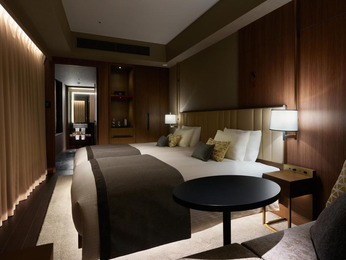 Mitsui Garden Hotel Roppongi Tokyo Premier Εξωτερικό φωτογραφία The photo shows a stylish hotel room featuring two beds with plush bedding and decorative pillows. The walls are made of wood, creating a warm and modern atmosphere. There are bedside lamps on each side of the beds providing soft lighting. A small ro
