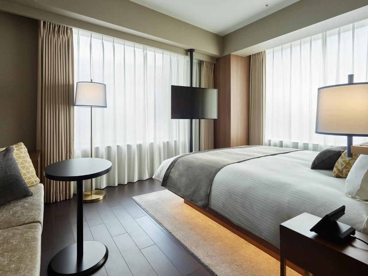 Mitsui Garden Hotel Roppongi Tokyo Premier Εξωτερικό φωτογραφία The photo shows a modern hotel room with a contemporary design. It features a large bed with crisp white linens, sitting against a wall with floor-to-ceiling windows covered by sheer curtains, allowing natural light to filter in. To the side, there's