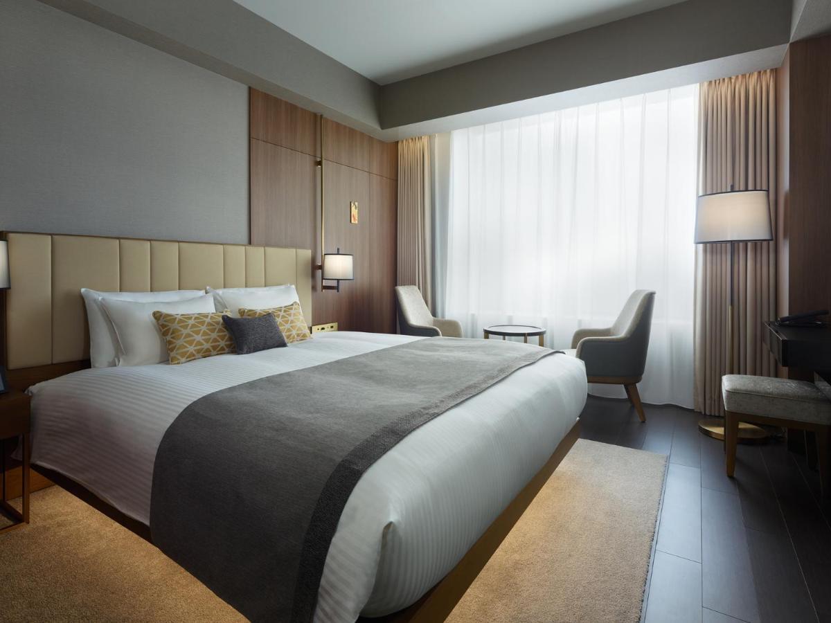 Mitsui Garden Hotel Roppongi Tokyo Premier Εξωτερικό φωτογραφία The photo shows a modern hotel room featuring a large bed with a neatly arranged white and gray bedding. The headboard is upholstered in a light color, adding to the room's contemporary design. On either side of the bed, there are bedside lamps provi