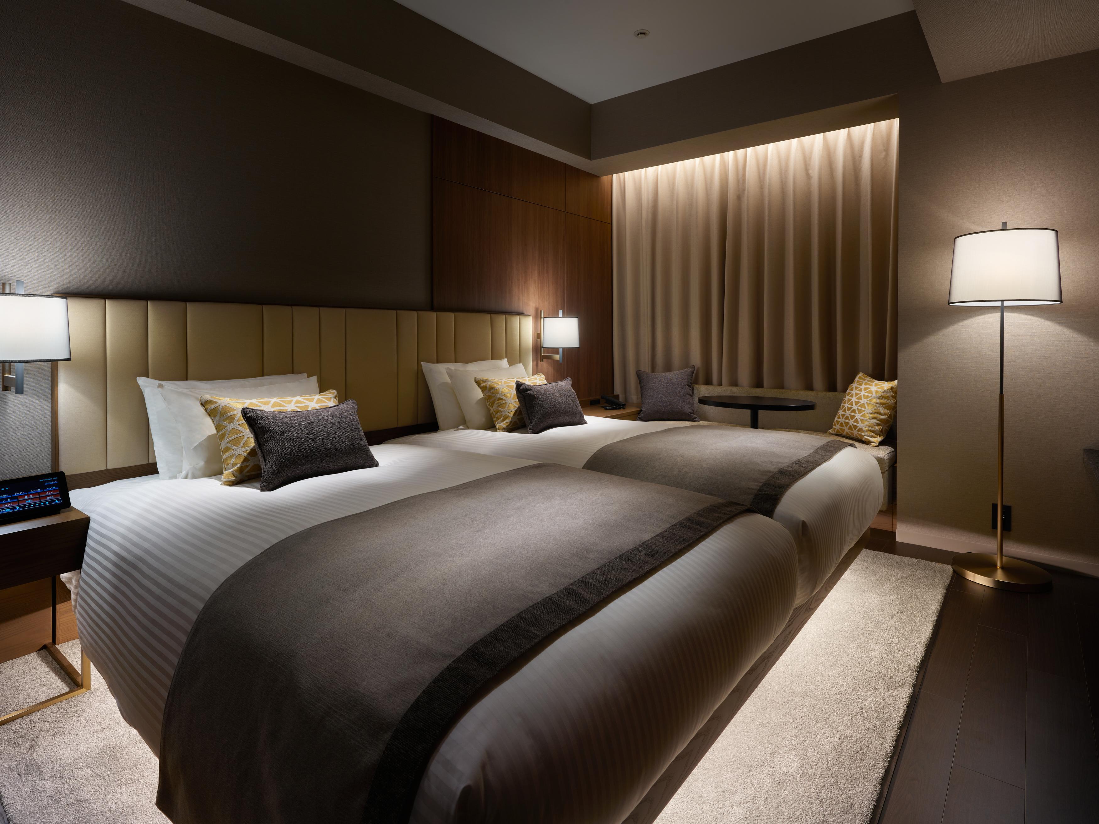 Mitsui Garden Hotel Roppongi Tokyo Premier Εξωτερικό φωτογραφία The photo shows a modern hotel room featuring two beds with elegant bedding in neutral colors. Each bed is adorned with decorative pillows. The room has a sophisticated ambiance with dim lighting, highlighted by table lamps on either side of the beds