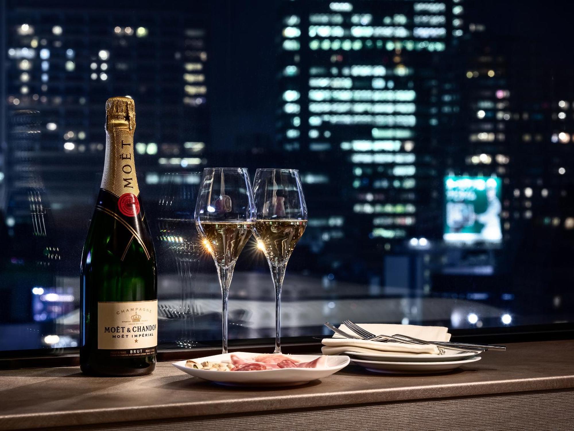 Mitsui Garden Hotel Roppongi Tokyo Premier Εξωτερικό φωτογραφία The photo features a bottle of champagne, specifically Moët & Chandon, alongside two filled champagne glasses. The table setting includes a small plate with a selection of food and neatly arranged utensils. In the background, there is a view of a cit
