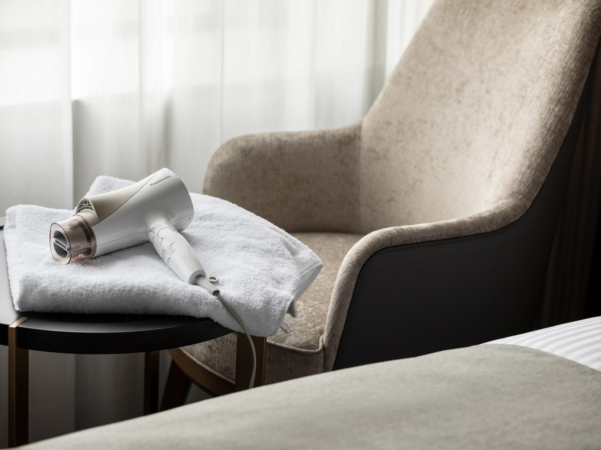 Mitsui Garden Hotel Roppongi Tokyo Premier Εξωτερικό φωτογραφία The photo features a cozy setup in a room. There is a soft chair in a neutral color positioned beside a small side table. On the table, a hairdryer is placed on a folded white towel. The background includes a light-colored curtain, letting in natural