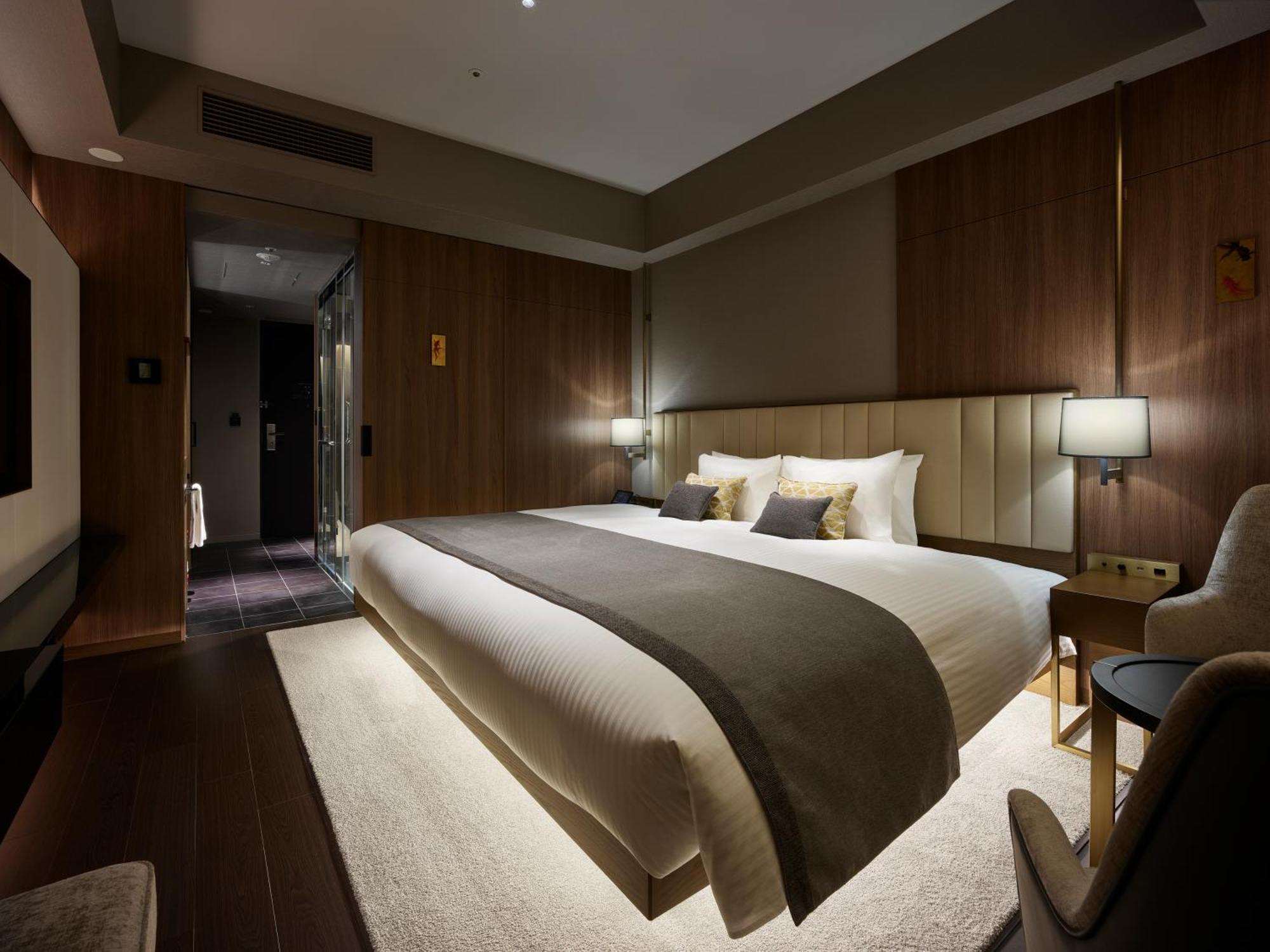 Mitsui Garden Hotel Roppongi Tokyo Premier Εξωτερικό φωτογραφία The photo shows a modern hotel room featuring a large bed with a neutral-colored duvet and a dark throw blanket. The headboard is upholstered, and there are two bedside lamps on either side of the bed. The walls have a warm wood paneling, contributin