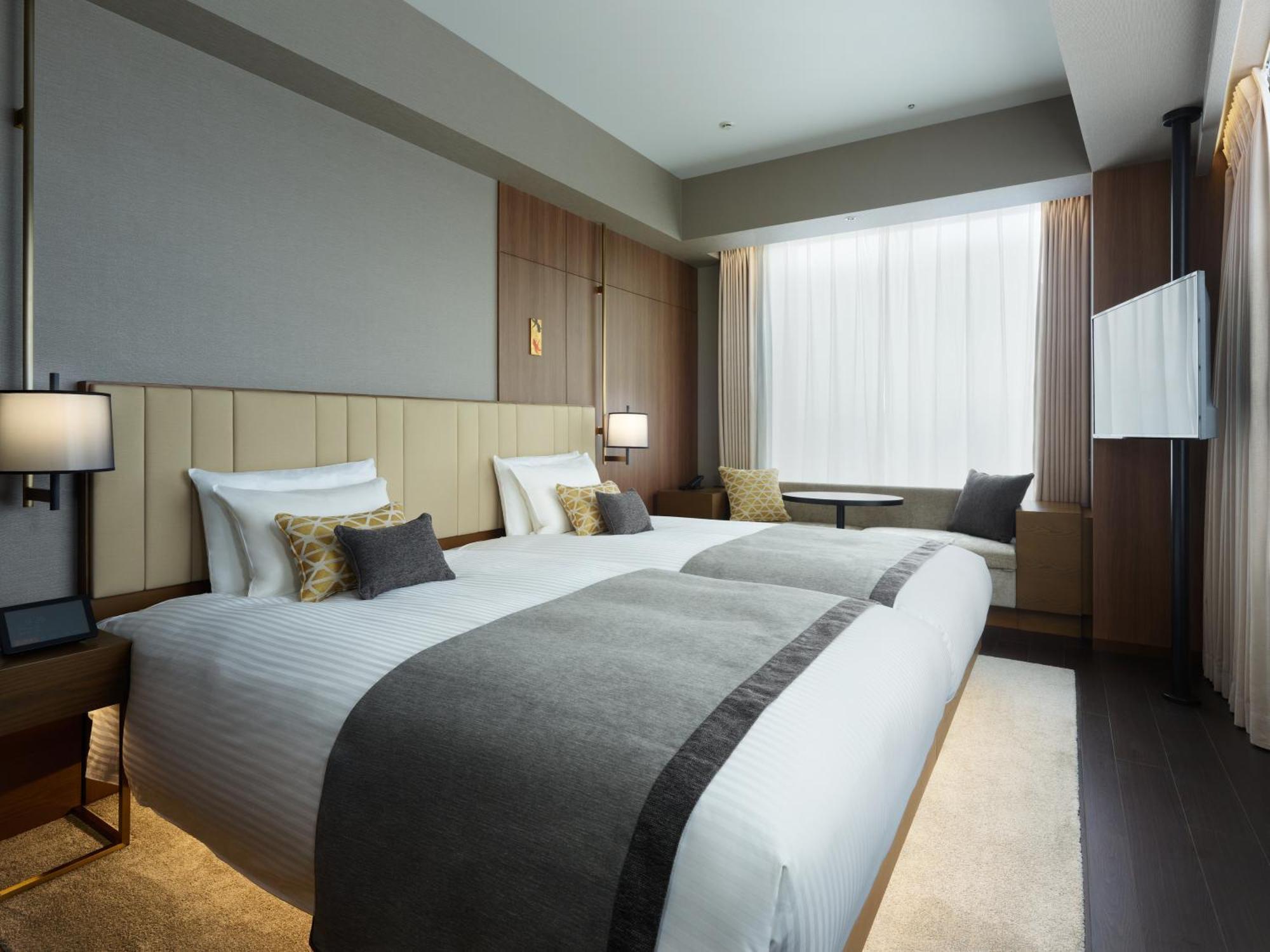 Mitsui Garden Hotel Roppongi Tokyo Premier Εξωτερικό φωτογραφία The photo shows a modern hotel room featuring two beds with white linens and decorative pillows. The room has a minimalist design, with neutral-colored walls and wooden accents. Natural light comes in through large windows, which are partially covere
