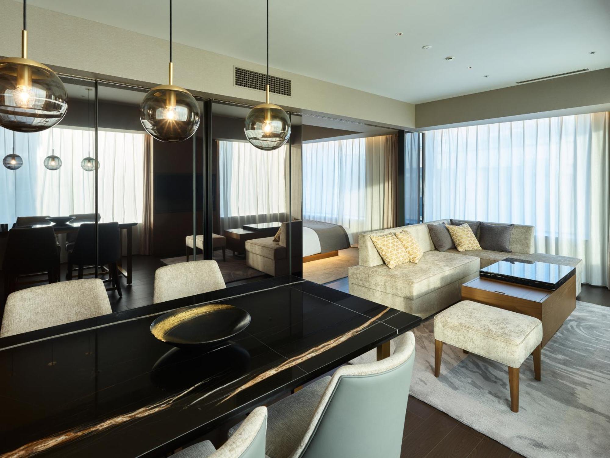 Mitsui Garden Hotel Roppongi Tokyo Premier Εξωτερικό φωτογραφία The photo shows a modern and stylish living area. It features a dining table with elegant chairs, a comfortable seating area with a light-colored sofa, and a coffee table. The room is well-lit by large windows draped with sheer curtains, allowing nat