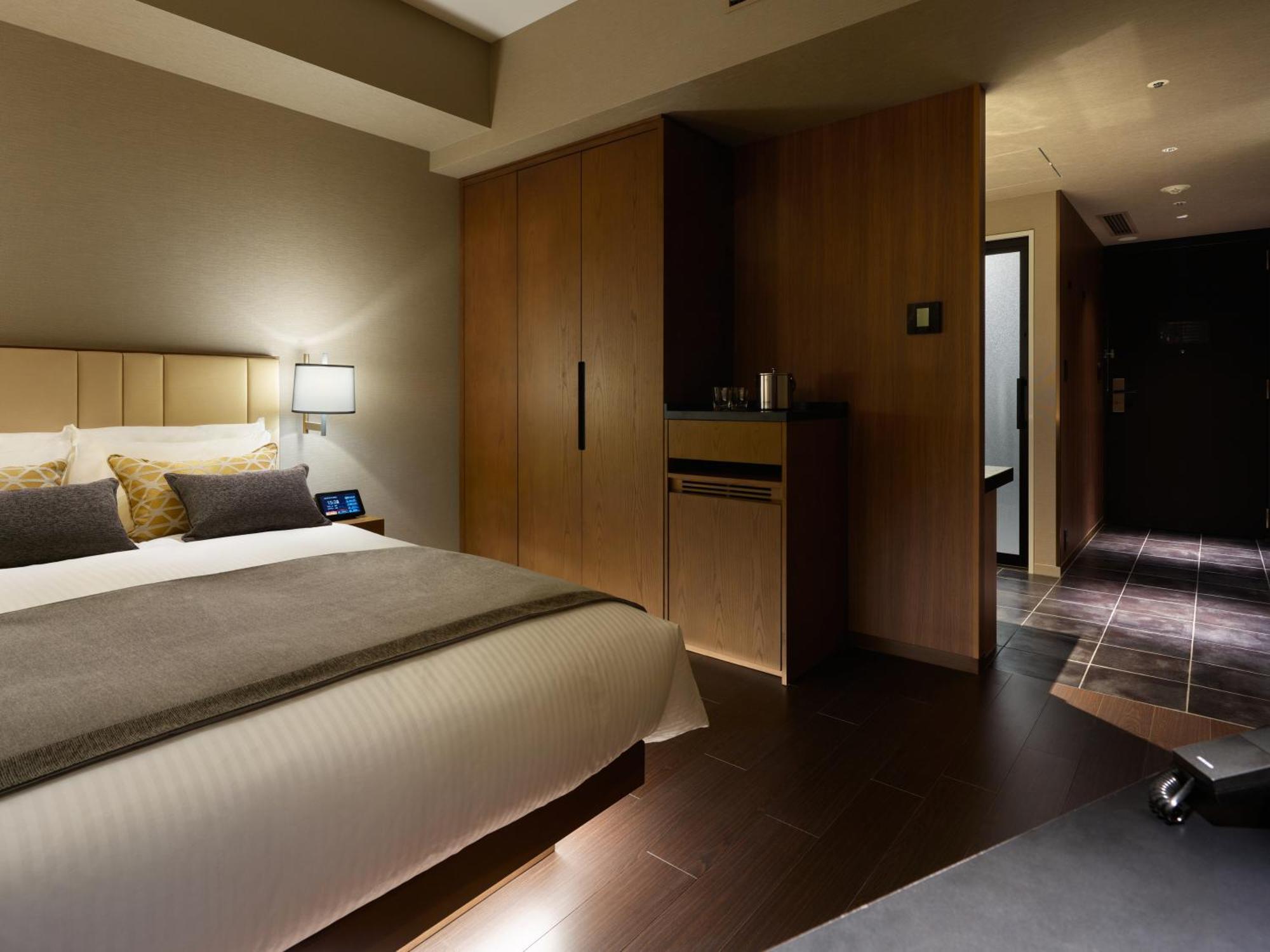 Mitsui Garden Hotel Roppongi Tokyo Premier Εξωτερικό φωτογραφία The photo shows a modern hotel room featuring a neatly made bed with decorative pillows. The room has wooden accents, including a wardrobe and cabinetry, contributing to a warm ambiance. A bedside lamp is on one side of the bed, and there's a small a